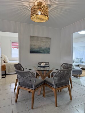 Un coin repas avec une table en verre entourée de chaises en osier, un luminaire suspendu au plafond et un tableau accroché au mur.