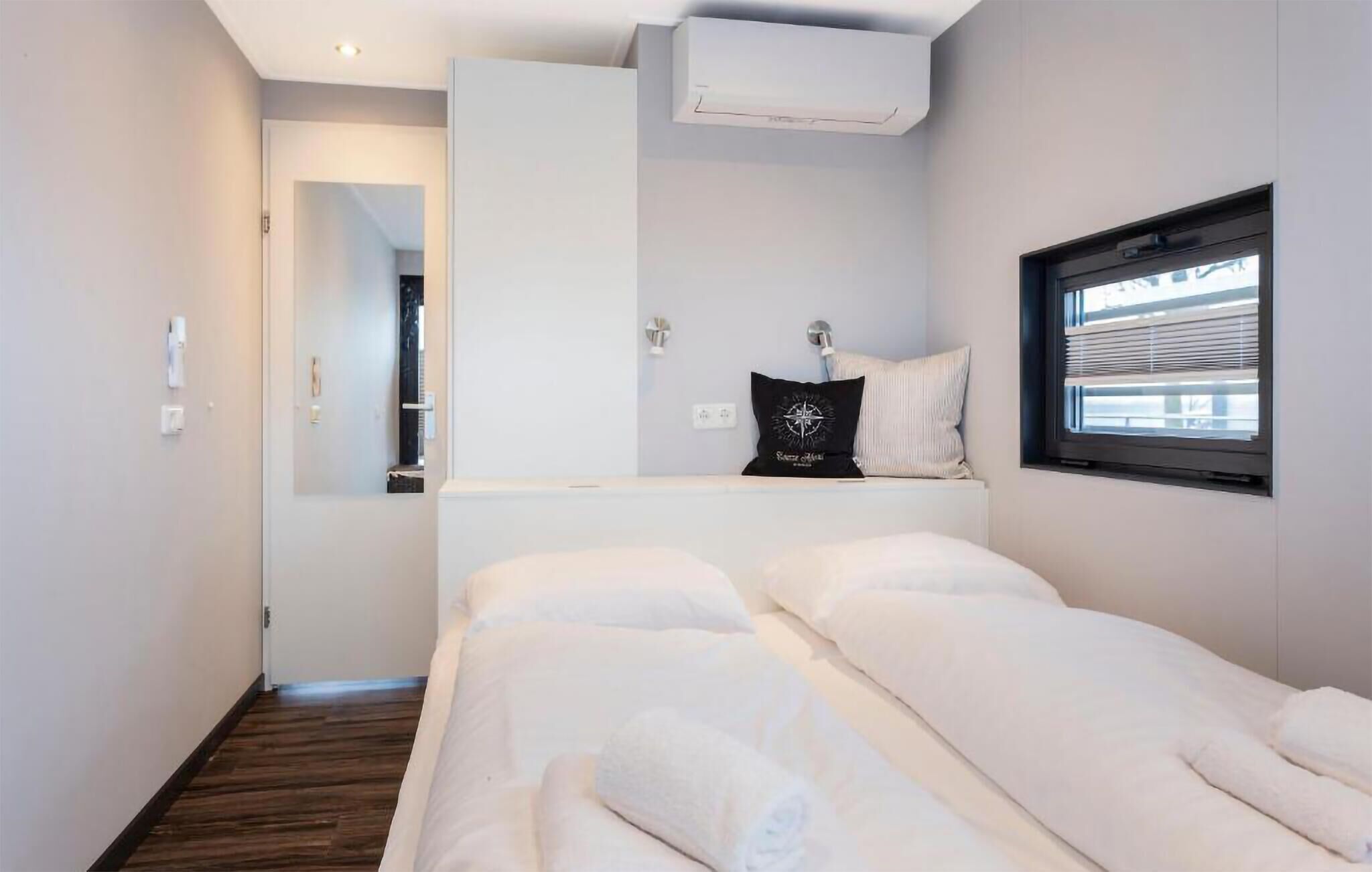 Ett hotellrum med en säng, ett fönster, en väggmonterad luftkonditioneringsanläggning och en liten hylla med en kudde.