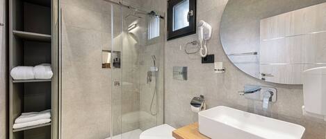 Un baño moderno con cabina de ducha de vidrio, un lavabo blanco y un mueble de tocador de madera.