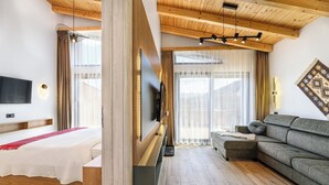 Een moderne hotelkamer met een houten plafond, een bed met een rode loper, een grijze bank, een aan de muur bevestigde televisie en een groot raam met transparante gordijnen.