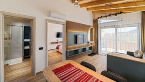 A modern living room with a wooden ceiling, a TV mounted on a wall, a dining table with chairs, and a view through large windows.