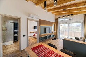 Uma sala de estar moderna com teto de madeira, televisão montada na parede, mesa de jantar com cadeiras e vista através de grandes janelas.