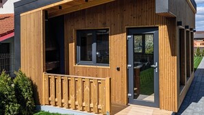 A modern, single-story house with a wooden exterior, a balcony, and a large sliding glass door.