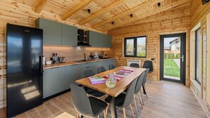 A modern kitchen with a black refrigerator, grey cabinets, and a wooden dining table with chairs.