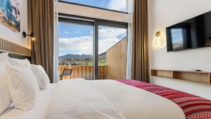 A hotel room with a large bed, a TV mounted on the wall, a view of mountains through a sliding door, and a wooden deck outside. - Selva Cabin 1 - The Trailhead Retreat (Zărnești)