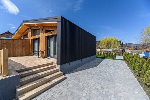 A modern house with a wooden deck, a black exterior wall, and a paved driveway.