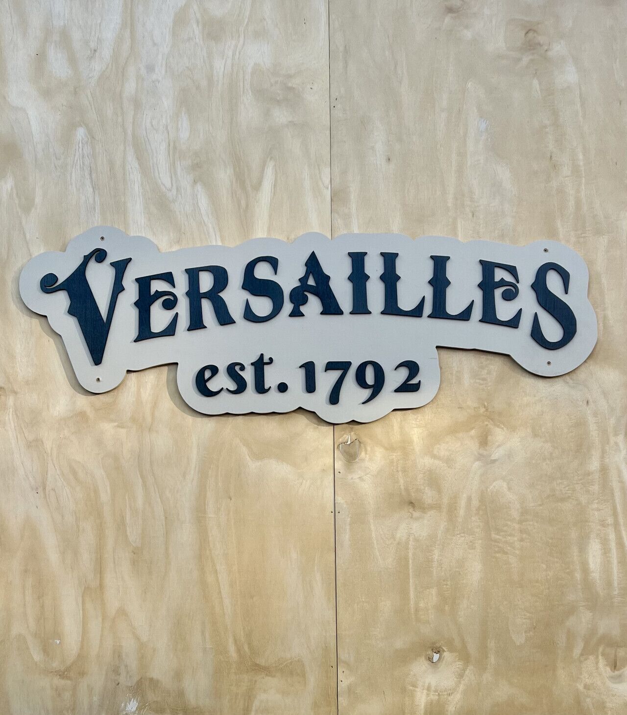A sign with the text 'VERSAILLES est. 1792' on a wooden background.