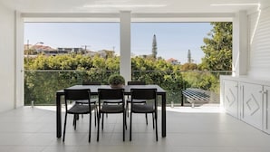 A modern balcony with a dining table and chairs, a potted plant, and a view of a residential area. - Ocean views: Steps from Sunrise Beach (Noosa)