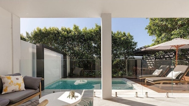 A modern outdoor pool area with a glass enclosure, lounge chairs, and a seating area with a coffee table. - Ocean views: Steps from Sunrise Beach (Noosa)