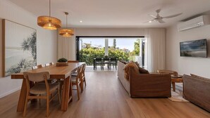 A modern dining area with a wooden table and chairs, a sofa, and a ceiling fan. - Ocean views: Steps from Sunrise Beach (Noosa)
