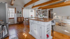 A kitchen with wooden beams, a central island, and a dining area with a white sofa. - NEW! Peaceful Truro retreat. Fire pit, outdoor shower, pet-friendly & close to Cape Cod’s beaches. (Truro)