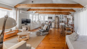A spacious living area with a wooden floor, a sofa, a coffee table, and a television. - NEW! Peaceful Truro retreat. Fire pit, outdoor shower, pet-friendly & close to Cape Cod’s beaches. (Truro)