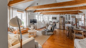 A spacious living area with wooden beams, a kitchen with white cabinets, and a dining area with a table and chairs. - NEW! Peaceful Truro retreat. Fire pit, outdoor shower, pet-friendly & close to Cape Cod’s beaches. (Truro)