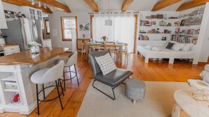 A spacious living area with a wooden floor, a dining table, a sofa, and a bookshelf. - NEW! Peaceful Truro retreat. Fire pit, outdoor shower, pet-friendly & close to Cape Cod’s beaches. (Truro)