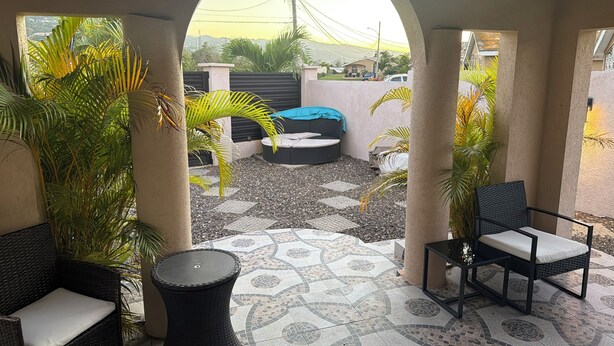Eine überdachte Terrasse mit Außenbestuhlung, einem gemusterten Boden und Blick durch einen Bogen.