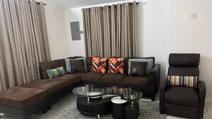 Ein Wohnzimmer mit einer Eckcouch, einem Glastisch und einem schwarzen Sessel.