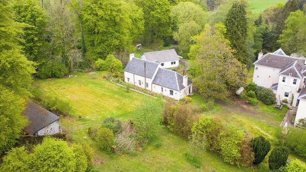 Une maison de campagne avec une grande pelouse et des arbres tout autour.