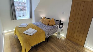 Une chambre à coucher avec un lit, une table de chevet, une porte en bois et une fenêtre avec des rideaux.