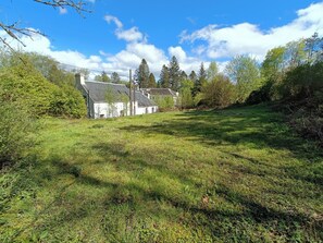 A grassy field with a white building and trees in the background.