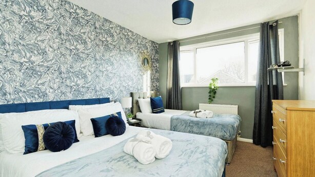 Une chambre d’hôtel avec deux lits, une commode, une fenêtre avec des rideaux et un mur dont le motif ressemble à du marbre.