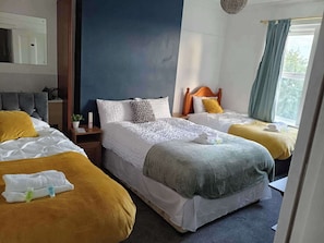 Habitación de hotel con dos camas, un espejo, una mesita de noche y una ventana con cortinas.