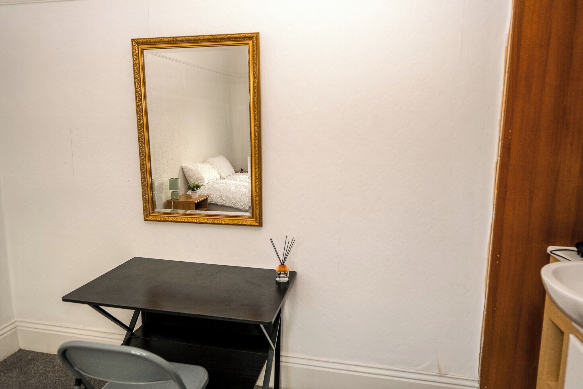 Een kleine kamer met een bureau, stoel en een spiegel aan de muur.