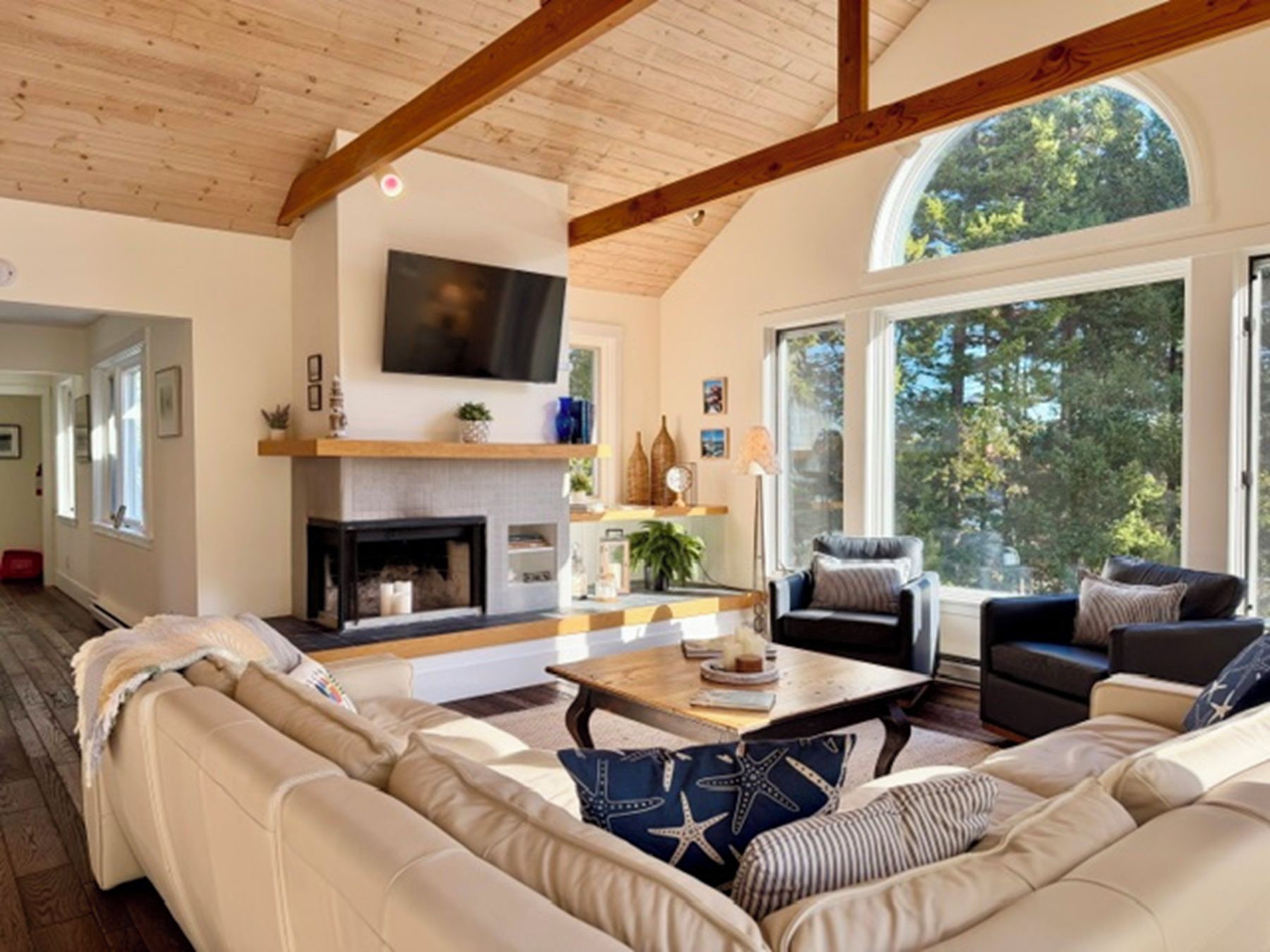A spacious living room with a fireplace, comfortable seating, and large windows offering a view of the outdoors.