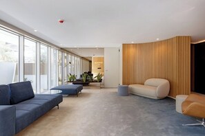 A modern living room with a sofa, ottoman, and a wooden accent wall. - Sal D’Ouro Atlantic Living | Gym & Garage (Vila Nova de Gaia)