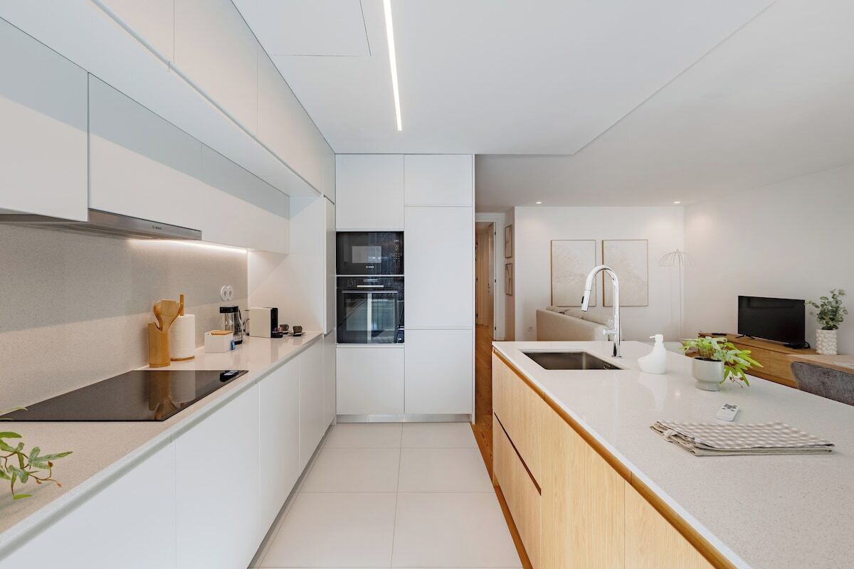 A modern kitchen with white cabinetry, a built-in oven, a black stovetop, and a wooden countertop.