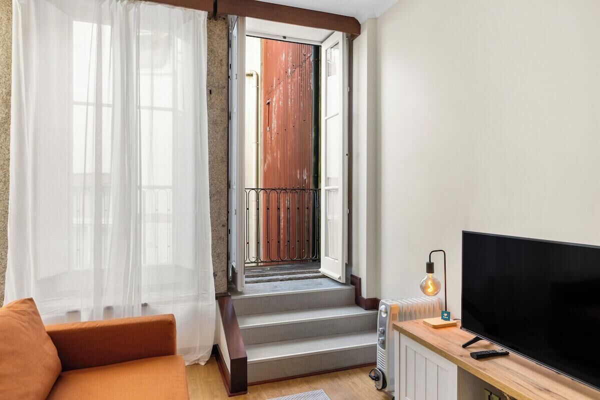 Un salón con sofá, televisor, radiador y una escalera que lleva a un espacio al aire libre.