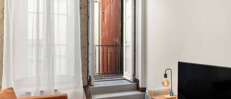 Un salón con sofá, televisor, radiador y una escalera que lleva a un espacio al aire libre.