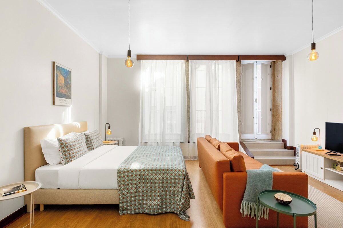 A modern hotel room with a bed, sofa, TV, and a view of the stairs.