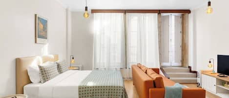 A modern hotel room with a bed, sofa, TV, and a view of the stairs.