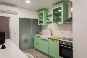 Cuina moderna amb armaris verds, taulell blanc, un rentatòries, una cuina i una porta de vidre que dona a la dutxera.