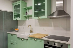 A kitchen with green cabinets, a white sink, a wooden cutting board, a stainless steel range hood, and a black stovetop. - Duque Central Stay | Walk to Rossio & Chiado (Lisbon)