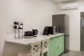 Een kleine keuken met een magnetron, koffiezetapparaat en wijnglazen op een wit aanrecht.