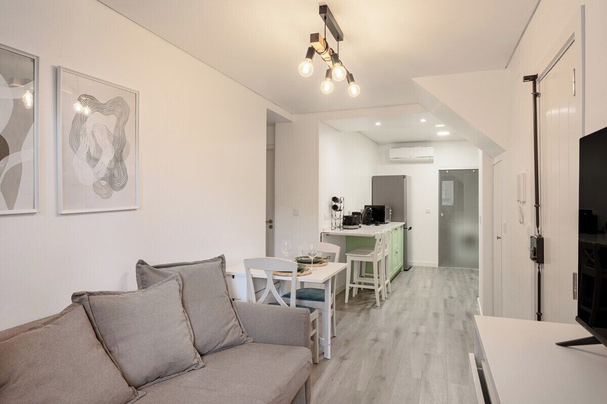 A modern living room with a sofa, a dining table, and a kitchen area in the background.