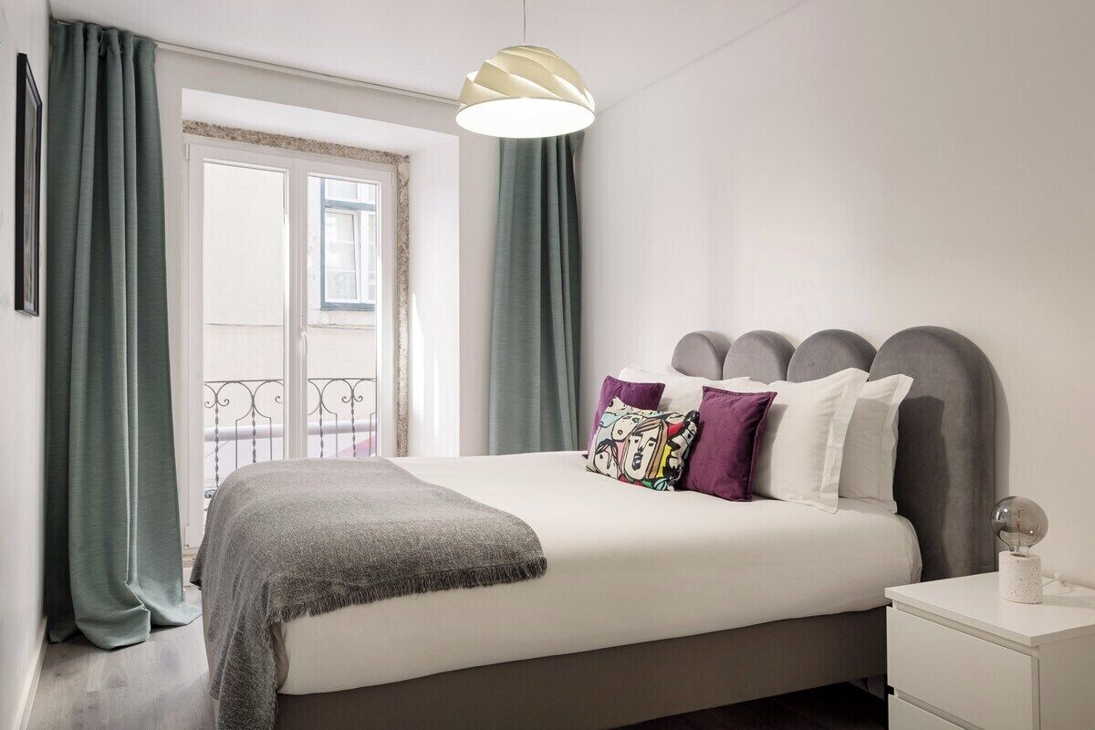 A neatly made bed with a grey headboard, a white bedside table, and a hanging light fixture.