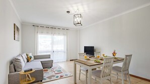A modern living room with a sofa, dining table, chairs, a TV, and a small side table. - Gaia Comfort Living | Balcony & Metro (Vila Nova de Gaia)