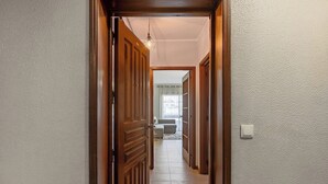 A hallway with wooden doors, a light fixture, and a view into a room with a sofa and a window. - Gaia Comfort Living | Balcony & Metro (Vila Nova de Gaia)