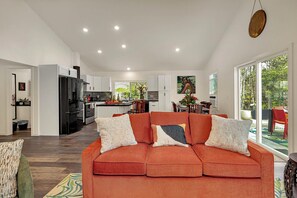 A modern living room with a sofa, a dining area, and a kitchen in the background.
