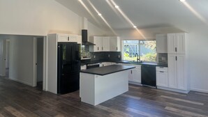A modern kitchen with white cabinetry, a black refrigerator, and a central island. - Charming 3-bedroom house in Volcano w/laundry & AC, perfect for your getaway! (Volcano)