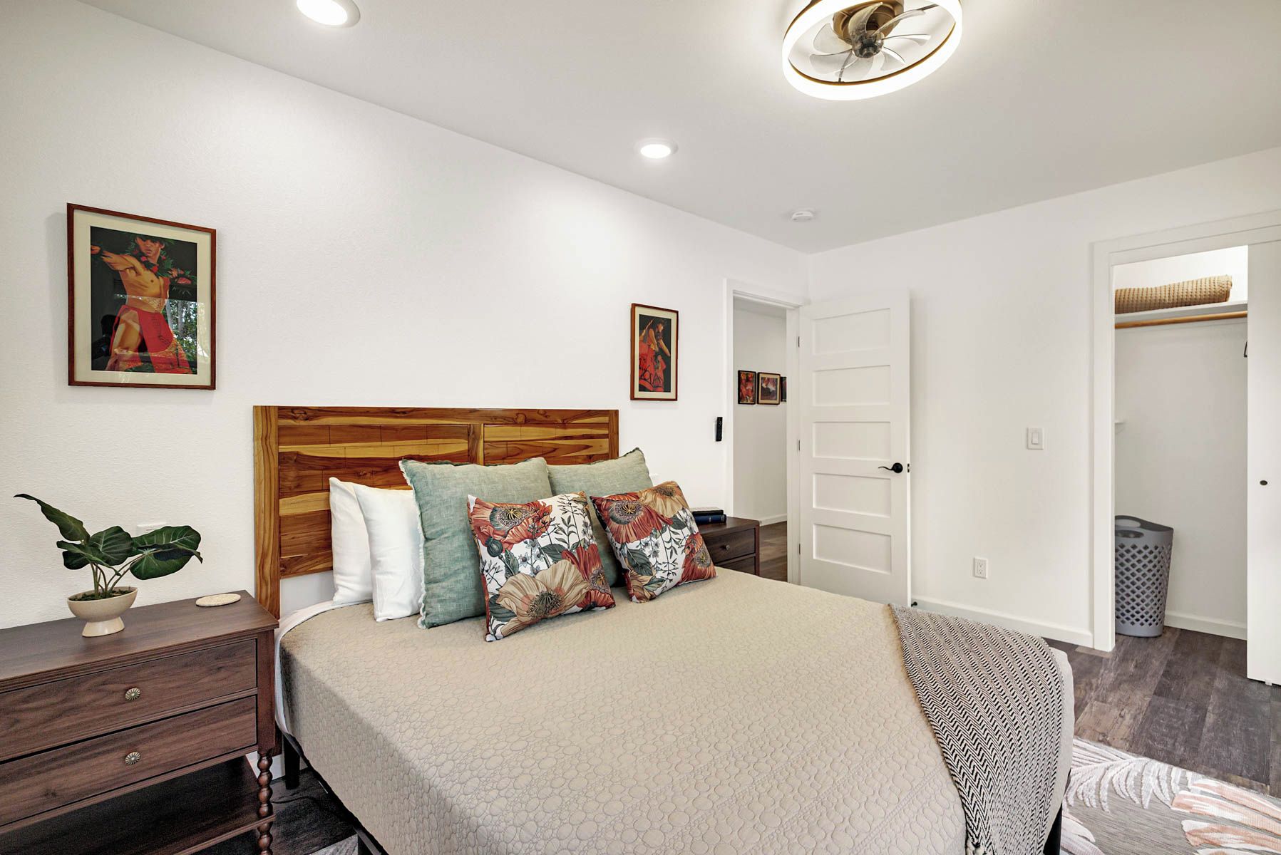 A bedroom with a wooden headboard, a bed with patterned pillows, a bedside plant, and a door leading to another room.