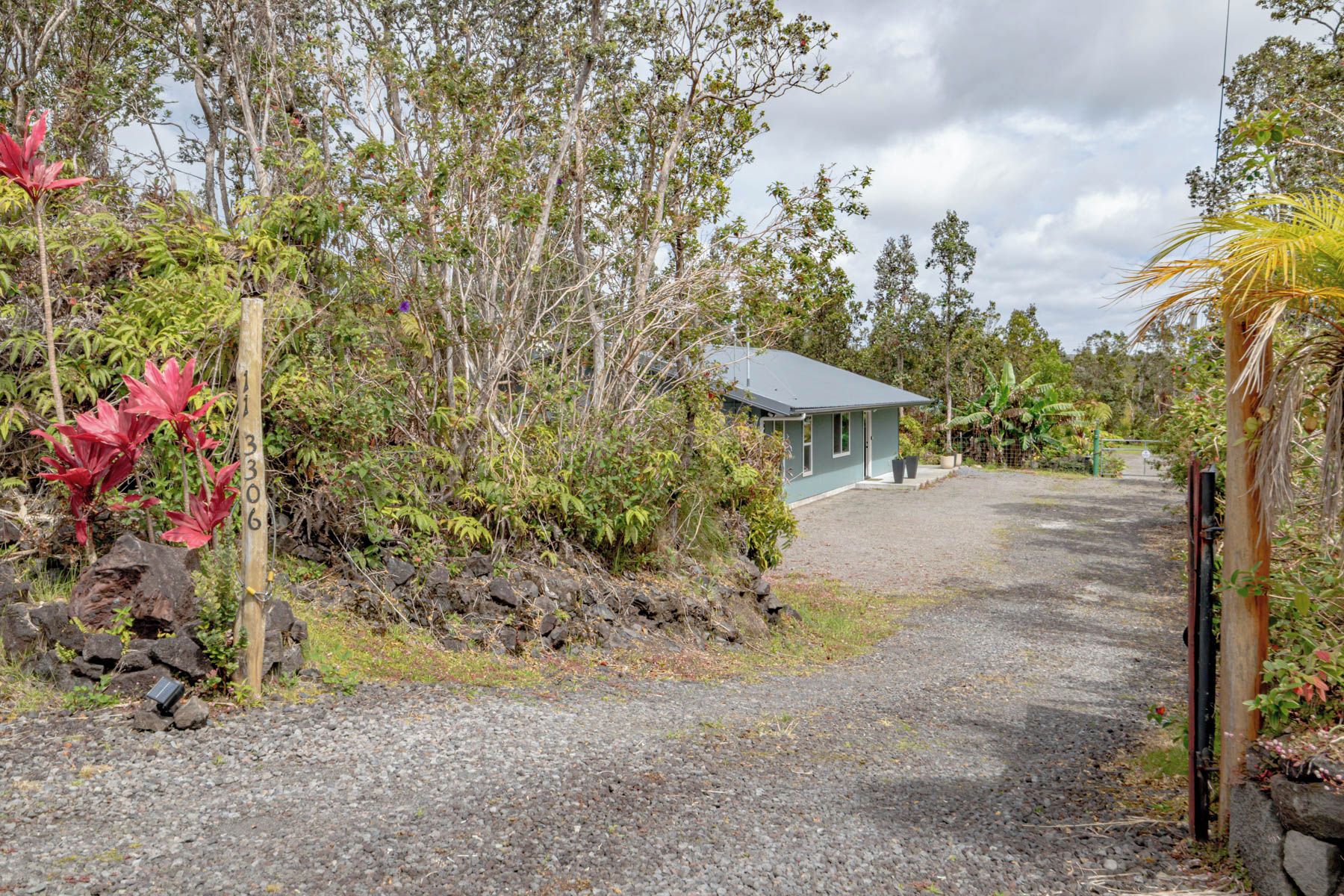 A gravel path leading to a small building with a metal roof, surrounded by dense vegetation and trees.
