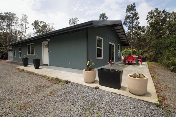 A modern two-story house with a flat roof, large windows, and a covered patio area with outdoor furniture.
