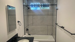 A bathroom with a bathtub, toilet, and a large mirror. - Charming 3-bedroom house in Volcano w/laundry & AC, perfect for your getaway! (Volcano)