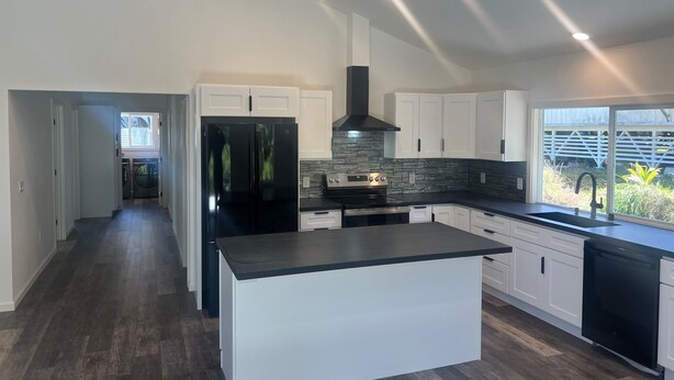 A modern kitchen with white cabinets, a black island, a stainless steel range, and a window with a view of greenery. - Charming 3-bedroom house in Volcano w/laundry & AC, perfect for your getaway! (Volcano)