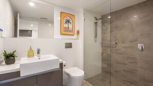 Une salle de bain moderne avec un lavabo blanc, des toilettes, une douche en verre et un tableau décoratif.