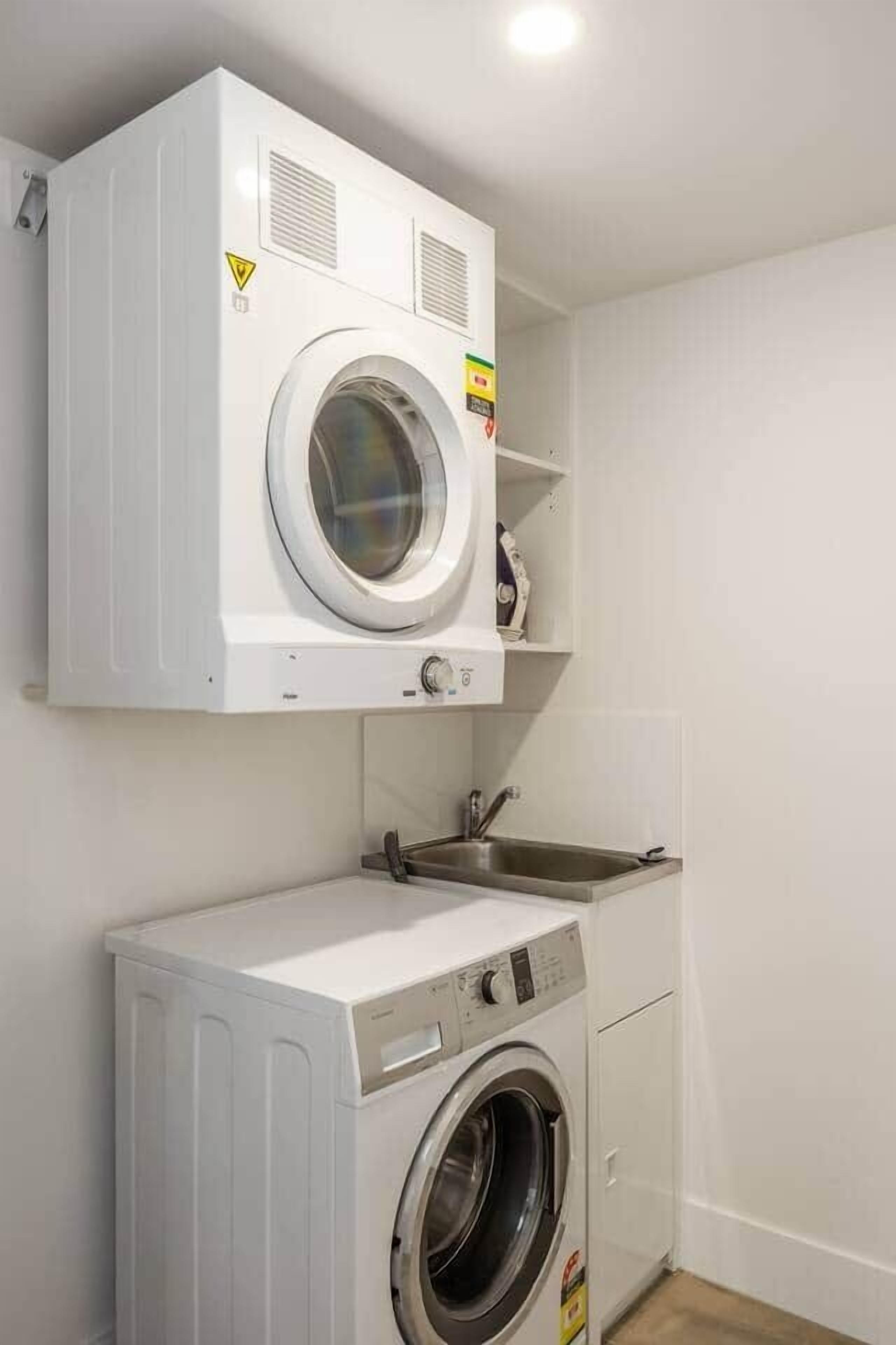 A compact laundry area with a washing machine and a dryer, a sink, and a shelf with a few items.