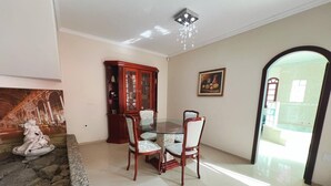 A dining area with a glass table and chairs, a stone fireplace, a wooden cabinet, and a painting on the wall. - Casa com Piscina em Cabeçudas , 80 metros da Praia (Itajaí)